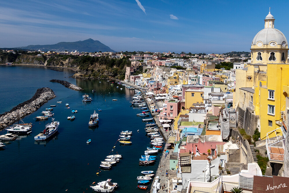 Procida - Blick auf Corricella
Die Bucht der Marina Corricella mit ihren bunten und ineinandergeschachtelten Häuschen in Würfelform gilt vielen Italienliebhabern als eine der schönsten des ganzen Landes. Fischer flicken Netze. Wäsche hängt zum Trocknen an Leinen. Auf den Tischen der Freiluftlokale dampfen Linguine mit Meeresfrüchten und andere Köstlichkeiten. Am selben Ort ließ Regisseur Michael Radford den Schauspieler Massimo Troisi im Film "Il Postino" mit Gedichten um die Gunst der schönen Beatrice werben; auch Matt Damon und Gwyneth Paltrow nippten in diesem Setting in "Der talentierte Mister Ripley" am Martini und blinzelten bei gleißender Sonne aufs Mittelmeer. laut sueddeutsche
Schlüsselwörter: Italien; 2024